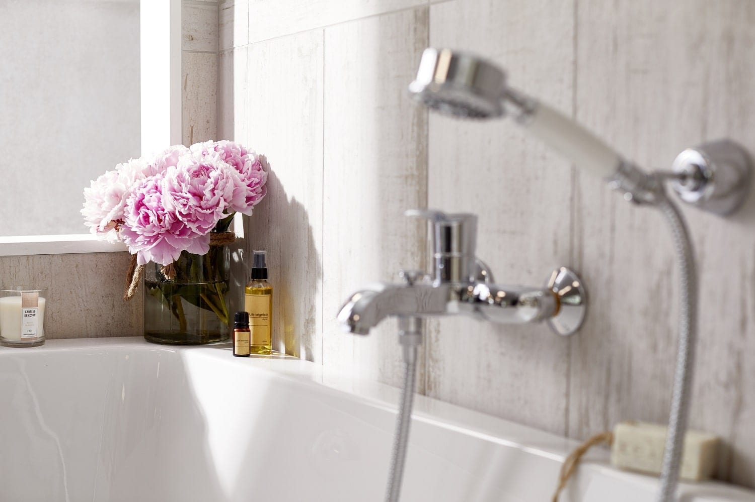 photo bouquet de pivoine dans un vase, bouteilles d’huile d’argan et d’huile essentielle de jasmin posés près d’une baignoire